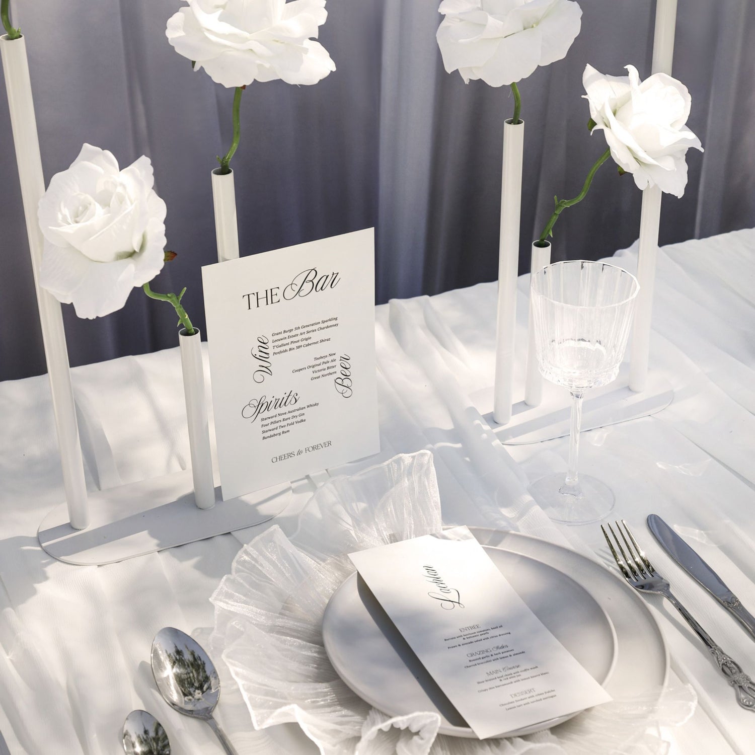 Table setting with white flowers, menu cards, and silverware on a white tablecloth.