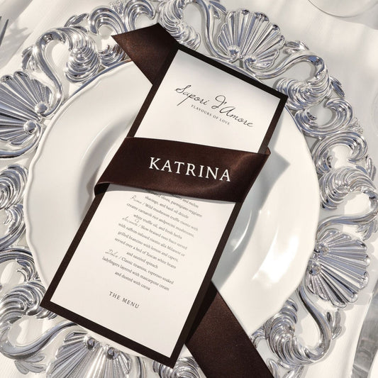 Decorative place setting with a menu and ribbon on an ornate plate.